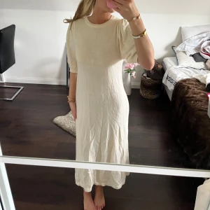 Ljusbeige stickad långklänning - Säljer en ljusbeige stickad långklänning med rund halsringning och korta puffärmar. Klänningen har en rak passform och är tillverkad i ett mjukt, stickat material som ger en avslappnad men stilren look. Den skulle behöva strykas nertill men superfin till sena sommarkvällar!!