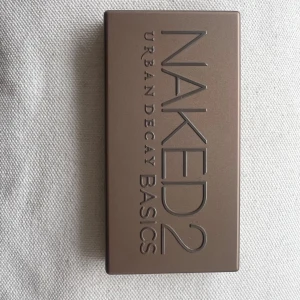 Naked2 Basics ögonskuggspalett från Urban Decay - Urban Decay Naked2 Basics är en kompakt ögonskuggspalett med sex matta nyanser i neutrala toner, perfekt för naturliga eller sotade looks. Paletten har ett smidigt fodral i beige-bronsig plast och inkluderar en stor spegel. Oanvänd men har ingen förpackning kvar. Den lilla paletten 