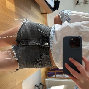 Svarta jeansshorts med fransar från Zara - Säljer ett par svarta jeansshorts från Zara med råa fransade kanter och klassisk femficksdesign. Shortsen är högmidjade och har en snygg, lite sliten tvätt. Perfekta för varma dagar och enkel att matcha med olika toppar.