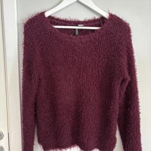Vinröd fluffig tröja från H&M Divided - Mysig vinröd långärmad tröja från H&M Divided. Tröjan har en fluffig, mjuk textur och rund halsringning. Perfekt för kyliga dagar när du vill vara både bekväm och snygg.