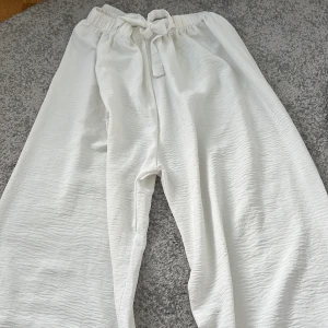 Vita vida byxor med knyt i midjan - Säljer ett par vita, vida byxor med resår och knytband i midjan. Byxorna har en luftig och avslappnad passform, perfekta för varma dagar. Materialet känns lätt och svalt mot huden. Perfekt för sommaren❤️