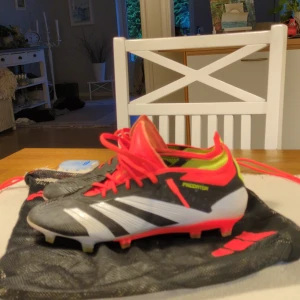 Adidas Predator Elite Ag/Fg fotbollsskor med röda detaljer - Säljer ett par Adidas Predator fotbollsskor i svart, vitt och rött med gula detaljer. Skorna har snörning och är designade för spel på gräs. Använda ungefär 10 gånger. Storlek EU 42. Priset kan sänkas i snabba förhandlingar 