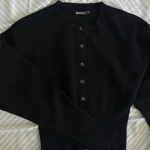 Svart kofta från Gina Tricot - En klassisk svart kofta från Gina Tricot med rund halsringning och knappar framtill. Tröjan har lång ärm och är enkel att matcha till olika outfits. Perfekt basplagg i garderoben.