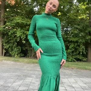 Grön långklänning med smock och volang - Säljer en snygg grön långklänning med smockad överdel och lång ärm. Klänningen har en volang nertill som ger extra rörelse och en tight passform upptill. Perfekt för dig som vill sticka ut med färg!