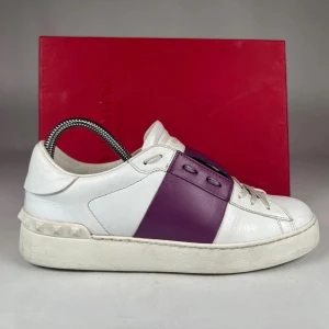 Valentino Open sneakers i vitt och lila - Säljer ett par snygga Valentino Open sneakers i vitt skinn med en bred lila skinnpanel över mitten. Skorna har rund tå, platt sula och klassisk snörning. Perfekta för dig som vill ha en stilren men ändå unik sneaker.