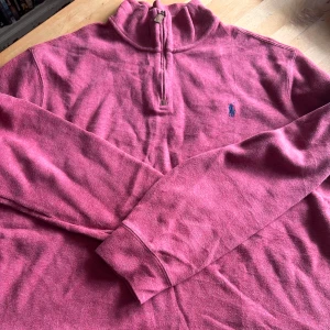 Vinröd halvzip tröja från Polo Ralph Lauren - Säljer en vinröd långärmad halvzip-tröja från Polo Ralph Lauren med broderad logga på bröstet. Tröjan har hög krage och dragkedja framtill. Perfekt för lager-på-lager och snygg till jeans eller chinos.