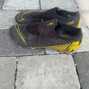 Fotbollsskor Nike Mercurial Vapor 360 fotbollsskor svart/gul - Säljer ett par Nike Mercurial Vapor 360 fotbollsskor i grå och gul med tydliga Nike-loggor och design. Skorna har mönstrad ovandel och dobbar för spel på gräs. Perfekta för dig som vill ha snabba och lätta skor på planen. Har dock tappat bort skosnörerna. Pris kan diskuteras vid snabb affär