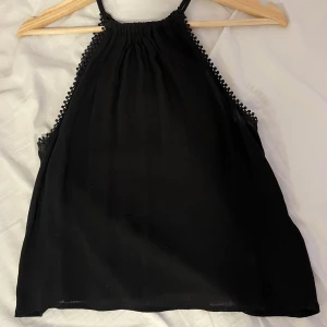 Svart halterneck topp - Svart, tunn och luftig halternecktopp med dekorativ kant. Perfekt för varma dagar och enkel att matcha med olika outfits.
