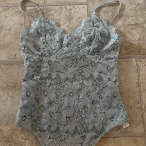Ljusblå spetsbody med blommönster - Säljer en ljusblå body i spets med tunna axelband och blommönster. Perfekt att styla under en kavaj eller till jeans för en trendig look. Bodyn har en feminin och romantisk känsla tack vare spetsen.