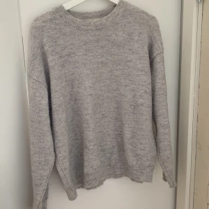 Ljusgrå stickad tröja från Gina Tricot - Mysig ljusgrå stickad tröja från Gina Tricot. Tröjan har rund halsringning, långa ärmar och ribbade muddar vid ärmslut.