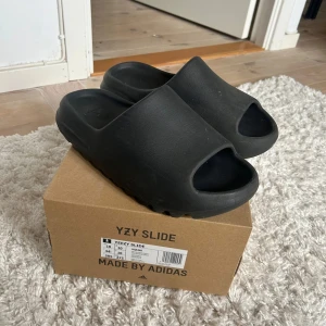 Svarta Yeezy Slides - Säljer ett par svarta Yeezy Slide med og box. Skorna är sparsmat använda utan sletage och fläckar. Obs skorna är i 44,5 men passar ungefär storlek 43. Skriv vid eventuella frågor eller funderingar.
