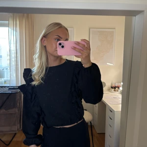 Svart volangtröja med puffärm - Säljer en svart långärmad tröja med volangdetaljer längs axlarna och puffiga ärmar. Tröjan har en stilren look som passar perfekt till både jeans och kjol. Materialet känns mjukt, tunt och bekvämt.