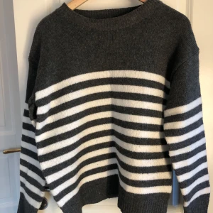 Grå och vit randig stickad tröja - Mysig stickad tröja i mörkgrått med vita ränder över bröstet och ärmarna. Tröjan har rund halsringning och långa ärmar. Tröjan passar som xs/s. Perfekt för kyligare dagar 🩶