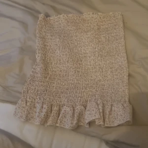 Tubtopp med blomigt mönster. - Supersöt beige blommig tubtopp  och volang längst ner.. Perfekt för en somrig och avslappnad look.