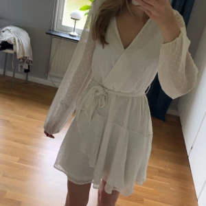 Vit klänning från Vero Moda - Söt vit klänning från Vero Moda i storlek xs, knytband i midjan och volangdetaljer. Klänningen har långärmade, lätt transparenta ärmar med diskret prickigt mönster och v-ringad hals. Tvättas såklart innan jag postar 🤍