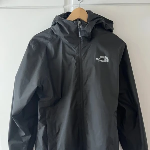 Svart vindjacka från The North Face - Säljer en svart vindjacka från The North Face med huva och dragkedja framtill. Jackan har en stilren design med logga på bröstet och är perfekt för blåsiga dagar. OBS jackan är lite stor i storleken, skulle säga att den passar S/M. Kan tänka mig att byta till en XS