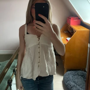 Vit blus med knappar - Säljer en söt vit blus med knappar framtill. Blusen är ärmlös med breda axelband och har en lätt utsvängd passform. Perfekt till sommaren och enkel att matcha med jeans eller kjol.
