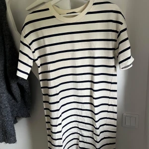 Vit och marinblå randig klänning från Zara - Vit klänning från Zara med marinblå horisontella ränder. Klassisk rund halsringning och korta ärmar. Perfekt för en avslappnad och stilren look. Tillverkad i mjukt bomullsmaterial.