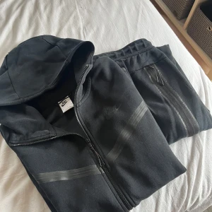 Svart Nike tech dress byxor + hoddie  - Ett helt set med både byxor och tröja. Äkta nike tech. Finns få tecken på användning men inget som är märkbart. Herr storlek M. Pris kan sänkas vid snabb affär!!!!! Skriv för frågor. 