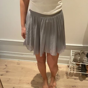 Ljusgrå plisserad kjol - Säljer en ljusgrå plisserad kjol med kort längd och flowig känsla. Kjolen har en bred resår i midjan och är tillverkad i ett tunt, lätt material som ger ett snyggt fall. Storlek 158. Men passar även mig som är small/medium