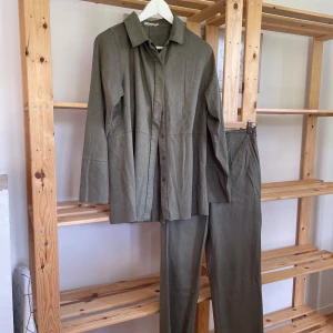 Olivgrön kostym  - Snygg olivgrön kostym med rak passform. Setet består av en långärmad skjortjacka med krage och matchande raka byxor. 