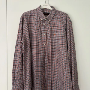 Rutig skjorta från Morris Stockholm - Säljer en klassisk rutig skjorta från Morris Stockholm i blått, rött och vitt. Skjortan har lång ärm, knappar framtill och en liten broderad logga på bröstet. Perfekt till jeans eller chinos.