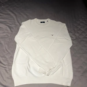 Vit stickad tröja från GANT - Säljer en stilren vit stickad tröja från GANT i storlek L. Tröjan har rund halsringning, diskret GANT-logga broderad på bröstet och är tillverkad i ett mjukt material. Perfekt för en klassisk och avslappnad look. Tröjan har dock en liten fläck på den vänstra armen, går nog att få bort den. Öppen för prisförslag!