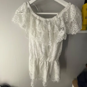 Vit spetsklänning från Gina Tricot - Superfin vit klänning i spets från Gina Tricot med offshoulder-modell och volangdetaljer. Klänningen har resår i midjan och är perfekt för sommarens alla tillfällen. Romantisk och luftig känsla med vackert spetsmönster.