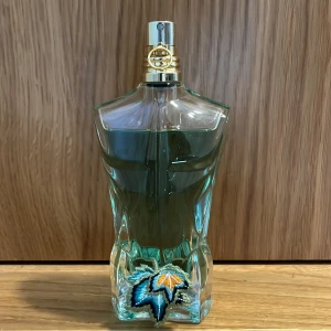 Jean Paul Gaultier Le Beau Paradise Garden EdP 75ml - Parfymflaska i form av en manlig torso i transparent grön glas med guldigt sprayhuvud. Märkt med broderad palm och solmotiv. Kommer i dekorativ rund förpackning med drakmotiv och blommor. Volym: 75 ml Eau de Parfum.