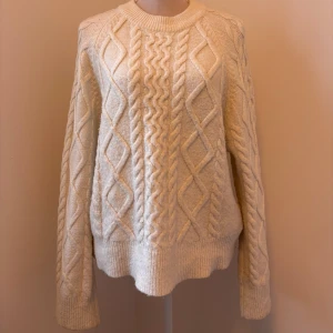 Vit stickad tröja från Gina Tricot - Säljer en mysig vit stickad tröja från Gina Tricot med ett snyggt flätmönster. Tröjan har långa ärmar. Är lite nopprig och liite grå vid slutet av ärmarna.