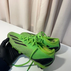 Gröna fotbollsskor från Adidas - Säljer ett par gröna fotbollsskor från Adidas med svarta detaljer och snörning. Skorna har en slitstark sula med dobbar för bra grepp på planen. Perfekta för fotbollsspelare som vill sticka ut på planen.