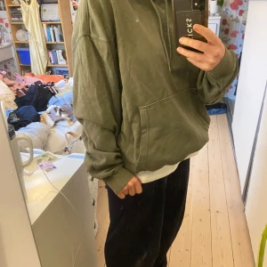 Grön hoodie från Weekday - Säljer en grön hoodie från Weekday i storlek S. Den har en klassisk design med en stor ficka framtill och en justerbar huva. Perfekt för en avslappnad stil.