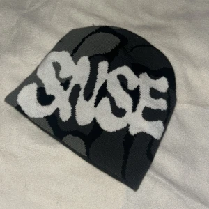 Grå och vit mössa med text - Snygg grå och vit mössa med stor text i graffiti-stil. Perfekt för att hålla sig varm och stilren under kyliga dagar.