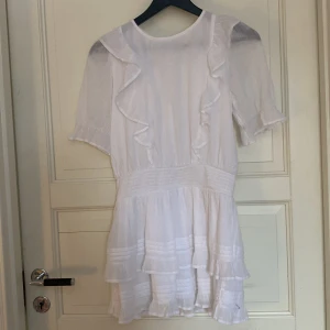 Vit klänning med volanger - Charmig vit klänning med volanger och korta ärmar. Perfekt för sommarens festligheter. Den har en luftig design med fina detaljer som ger en romantisk känsla. Använd endast en gång!