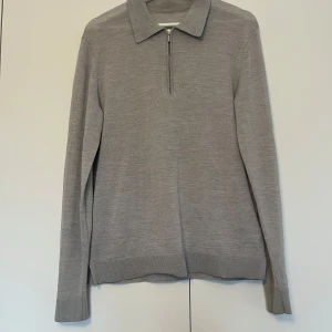 Grå tröja med dragkedja från Tiger of Sweden, tar bud! - Stickad tröja i merinoull från Tiger of Sweden. Quarter zip med krage i ljusgrå färg. Bra skick, med ett reparerat hål som bild visar. Även tagen har fallit av. Storlek M, sitter rätt så normalt i storlek. Köpt på Volt för ca 1600 kr. Bara att höra av sig vid frågor! Tar Bud!