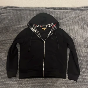 Svart huvtröja från Burberry - En fin svart zip hoodie från burrbery med ett unikt rutigt tyg på insidan. Storlek Xl men passar även L.
