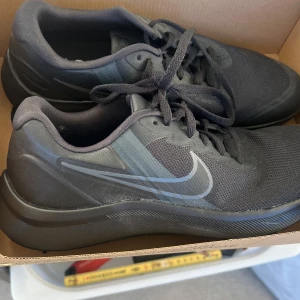 Svarta Nike sneakers - Säljer ett par svarta Nike sneakers med snörning. Skorna har en stilren design med Nike-loggan på sidan och en bekväm sula. Perfekta för vardagsbruk och träning.