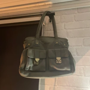 Grön  handväska med fickor - Snygg grön handväska med två framfickor som har metallspännen. Väskan har dubbla handtag och en stilren design, perfekt för att bära med sig det nödvändigaste. Aldrig använd💕