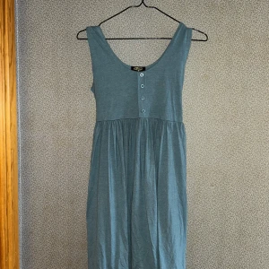 Blå ärmlös klänning med knappar - Snygg blå ärmlös klänning från Cation med knappar framtill och knytband i ryggen. Perfekt för en avslappnad stil. Klänningen har en passform som kan justeras med band i ryggen den och är gjord i ett mjukt material.