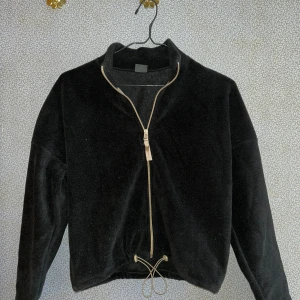 Svart fleecejacka  - Säljer en mysig svart fleecejacka från Bershka. Jackan har en dragkedja framtill och en hög krage. Perfekt för kyliga dagar när du vill hålla dig varm och bekväm. Den har en justerbar dragsko i nederkanten för en anpassad passform.