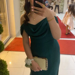 Grön axelbandslös långklänning - Elegant grön långklänning med offshoulder-design och draperad halsringning. Perfekt för festliga tillfällen med sin smickrande passform och stilrena look. Endast använd en kväll💗, priset går att diskuteras!! Klänningen är köpt för 1300kr💟💗