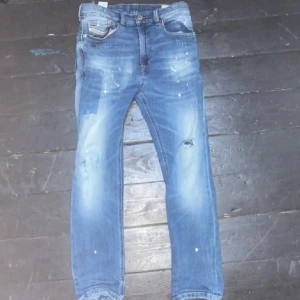 Blå jeans från Diesel - Snygga blå jeans från Diesel med slitna detaljer och en cool tvätt. De har en klassisk femficksdesign och en läderpatch med Diesel-logga på baksidan. Perfekta för en avslappnad stil.