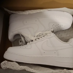 Vita Nike Air Force sneakers - Säljer ett par klassiska vita Nike Air Force sneakers. De har en stilren design med snörning och perforerade detaljer på tån för extra ventilation. Perfekta för en casual look.