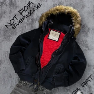 Mörk Blå jacka med päls från Abercrombie & Fitch - Säljer en snygg marinblå jacka från Abercrombie & Fitch med quiltat rött foder och pälsdetaljer på huvan. Lite lila innanför dragkedjan men inget man tänker på när man har på sig den. Jackan har dragkedja och knappar framtill, samt ribbade muddar vid ärmslut. Perfekt för kyliga dagar! Storlek M 