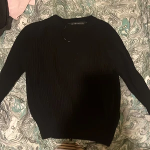 Svart tröja från The Black Label Collection - Snygg svart tröja från The Black Label Collection. Tröjan har en enkel design med långa ärmar och rund halsringning. Perfekt för en stilren look.