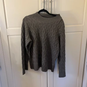 Grå stickad tröja - Säljer en mysig grå stickad tröja med ett vågigt mönster. Tröjan har långa ärmar och en rund halsringning. Perfekt för kyliga dagar!