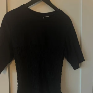 Svart topp från Divided - Säljer en svart topp från Divided med en smockad design som ger en snygg textur. Toppen har korta ärmar och en rund halsringning. Perfekt för en stilren look. 🖤