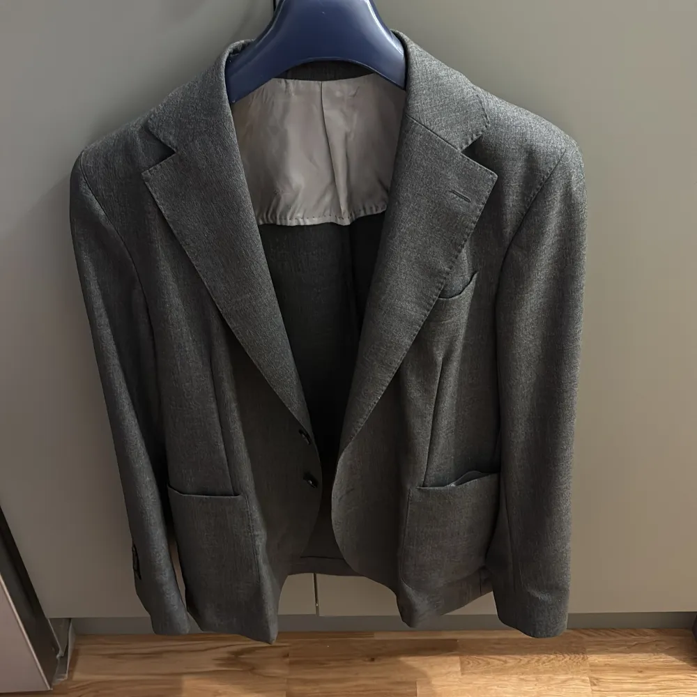 Elegant grå kavaj från Oscar Jacobson med klassisk design. Kavajen har två knappar framtill och fickor på sidorna. Perfekt för en stilren look.. Puvut & Bleiserit.