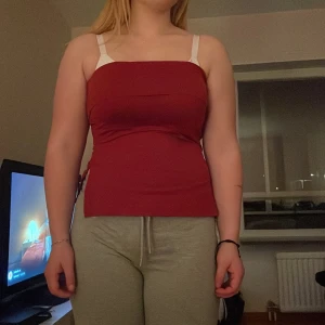 Röd tubtopp - Snygg röd tubtopp med vita axelband. Perfekt för sommardagar eller en kväll ute. Toppen har en tight passform som framhäver figuren.