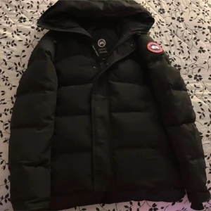 Svart dunjacka från Canada Goose - Säljer en svart dunjacka från Canada Goose med huva och dragkedja. Jackan har en klassisk pufferdesign och är perfekt för kalla vinterdagar. Märkeslogga på ärmen ger en exklusiv touch. Pris kan även minskas me nån hundra vid snabbt köp”